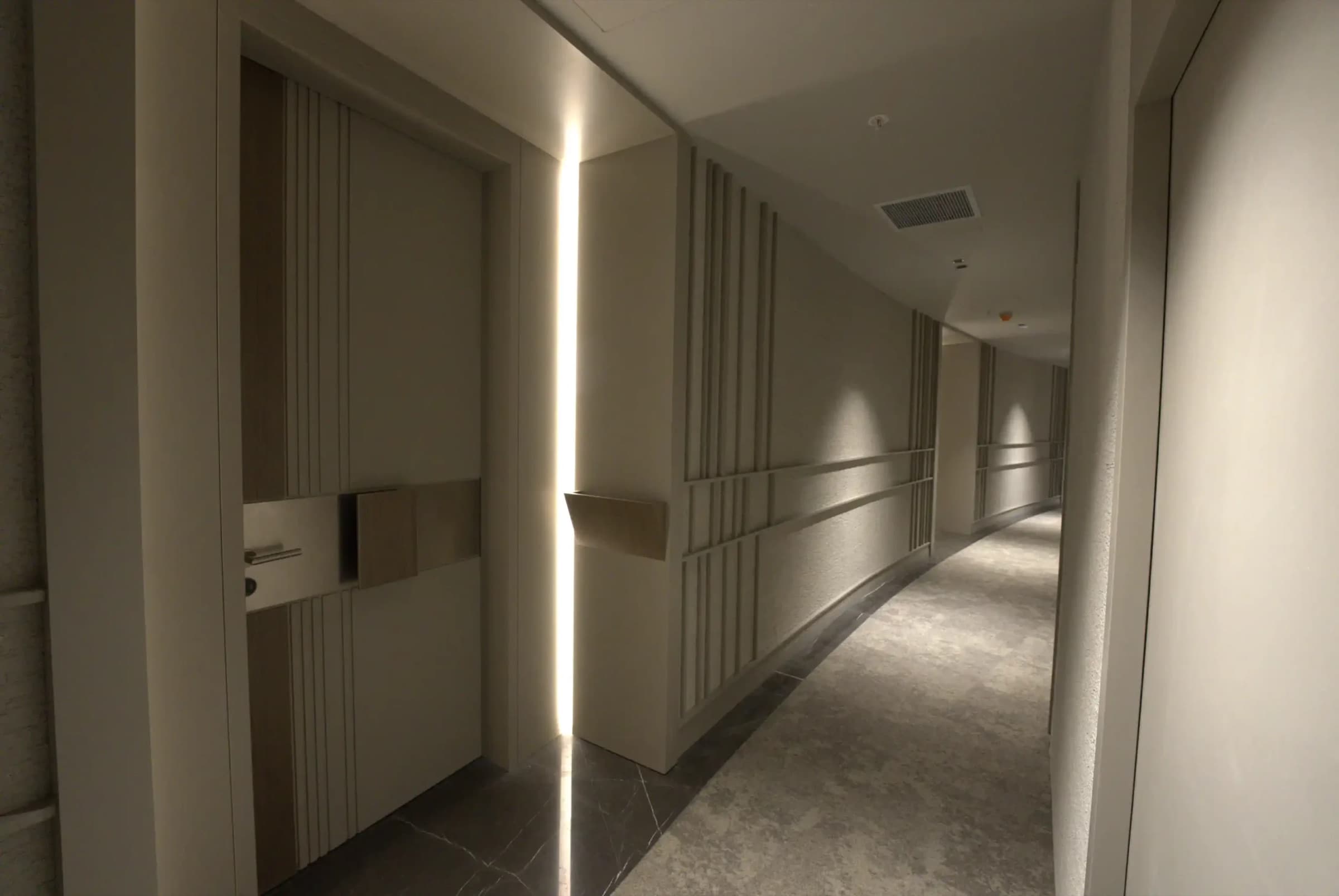 Curved residents' corridor on a residential floor, lit along one wall, with stone flooring and panelled apartment doors