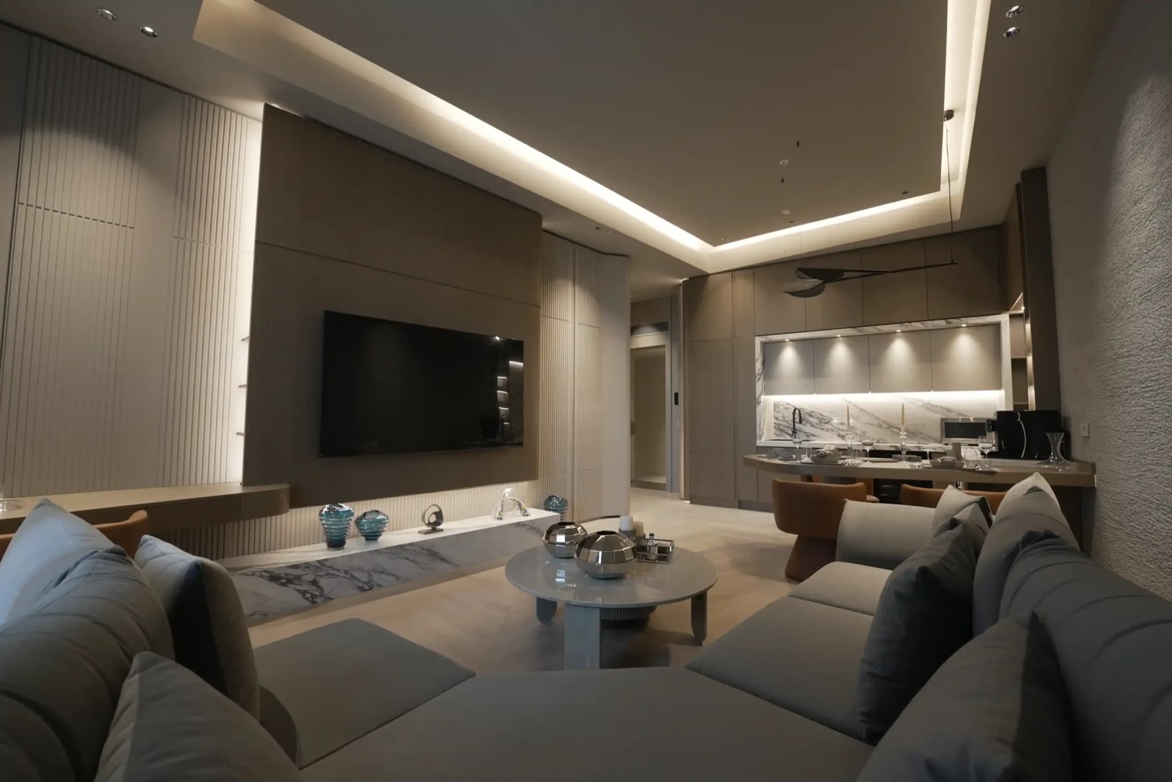 Living room looking through to the open kitchen, with a marble console below the television and a coved lighting recess