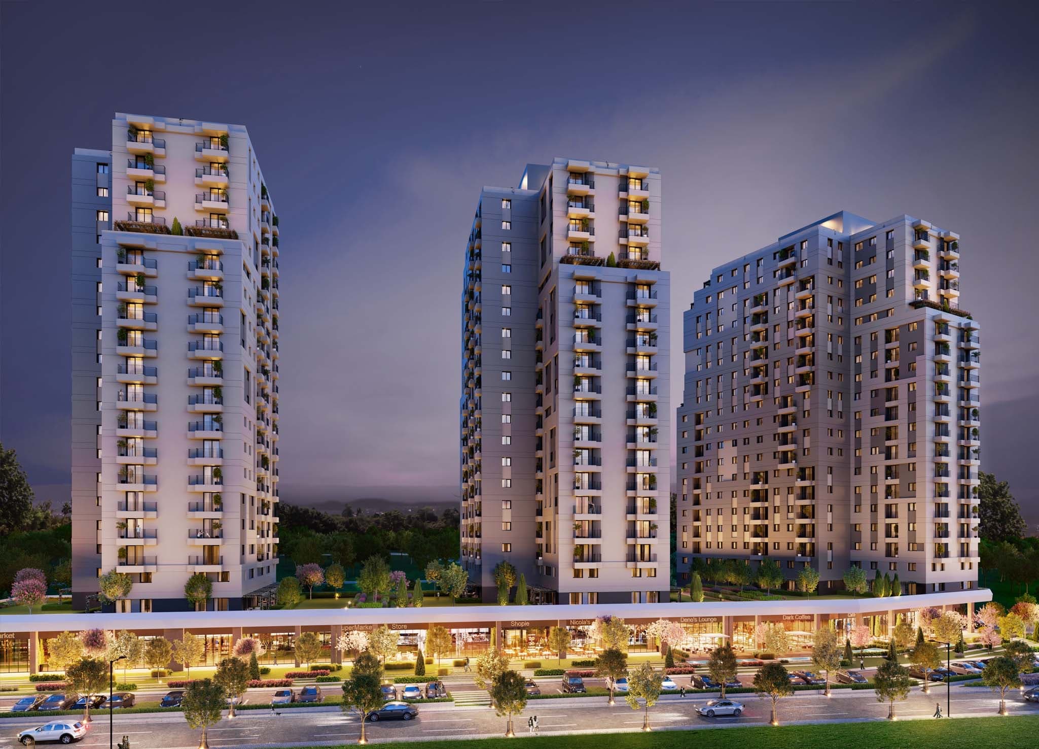 Night render of the development's three lit residential blocks above a long ground-floor retail street with a supermarket, shops and cafés, seen across a landscaped boulevard with parked cars — artist's impression