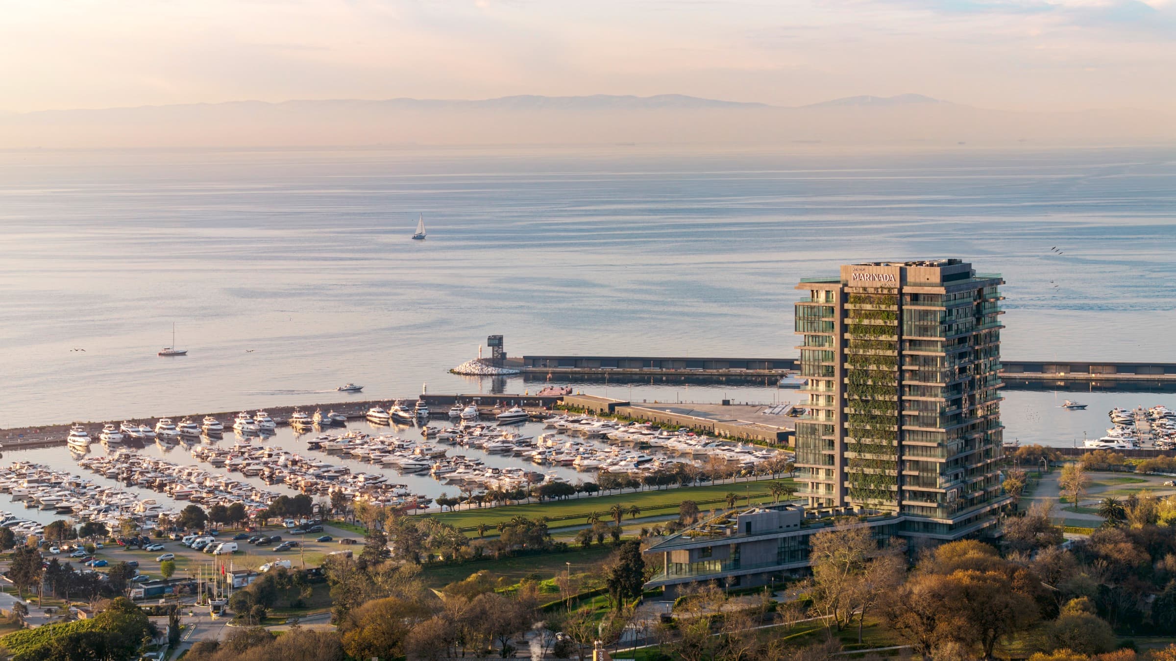 Ataköy Marinada Residence kıyının üzerinden: kule Ataköy Marina'nın başında duruyor, yüzlerce motor yat yerlerinde bağlı, dalgakıran Marmara Denizi'ne uzanıyor ve karşı kıyıda tepeler görünüyor