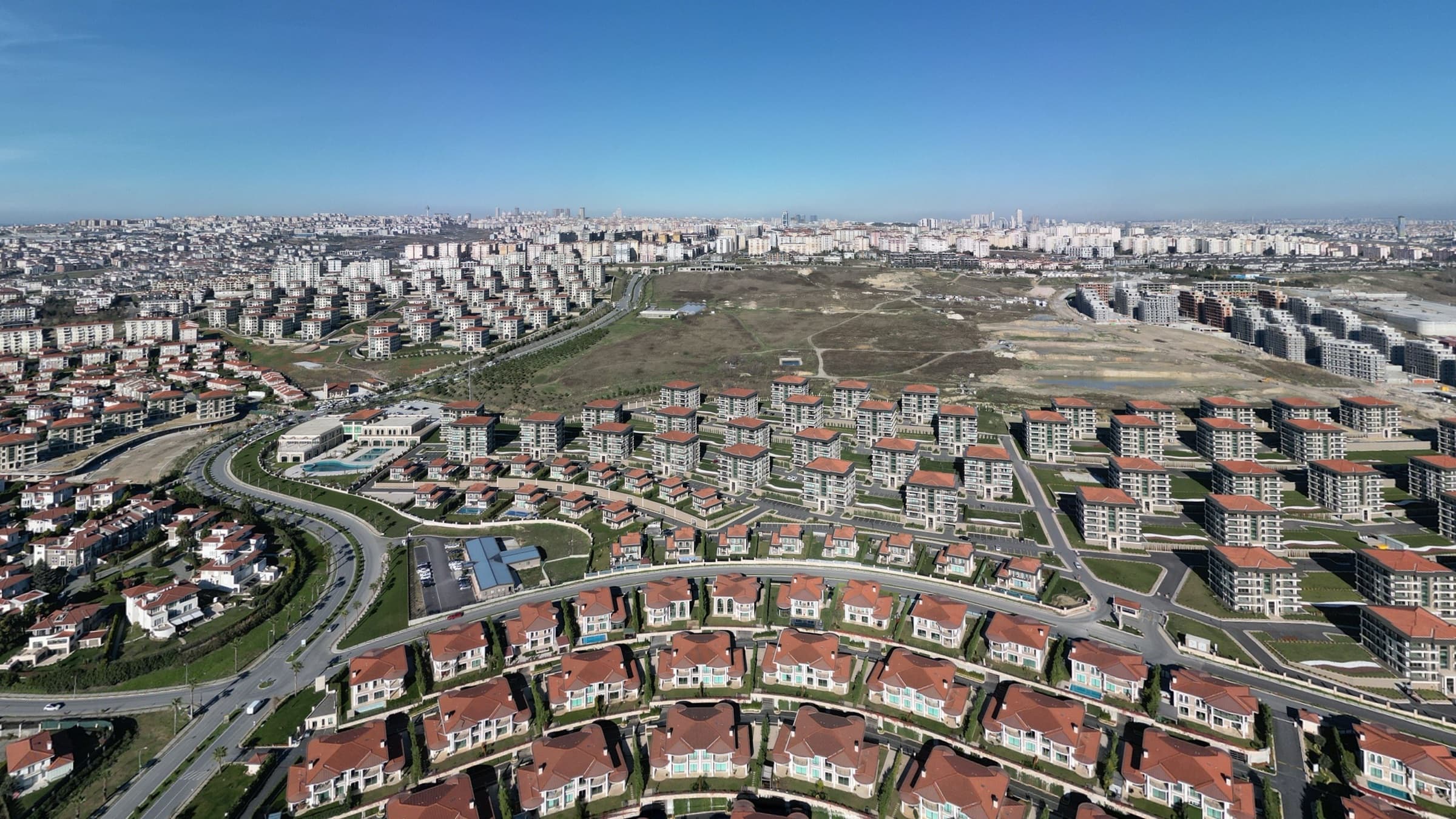 Yamaç boyunca kıvrılan Deniz İstanbul villa sokakları; her evin kendi bahçesi, birkaçında havuz, arkalarında kasabanın apartman blokları ve daha ötede İstanbul silueti.