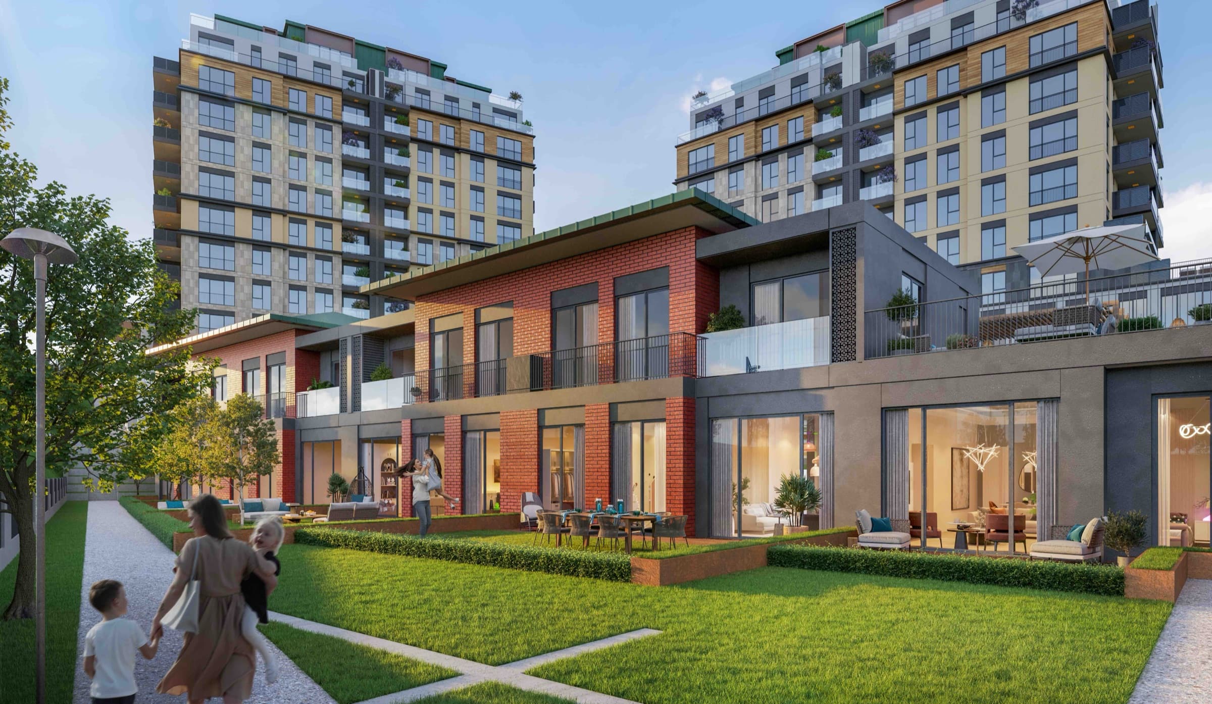 Render of the social building at Ebruli Kayaşehir seen across the lawn: a low block with a glazed, lit ground floor and terracotta panelling, with a woman and a child walking toward it along the path