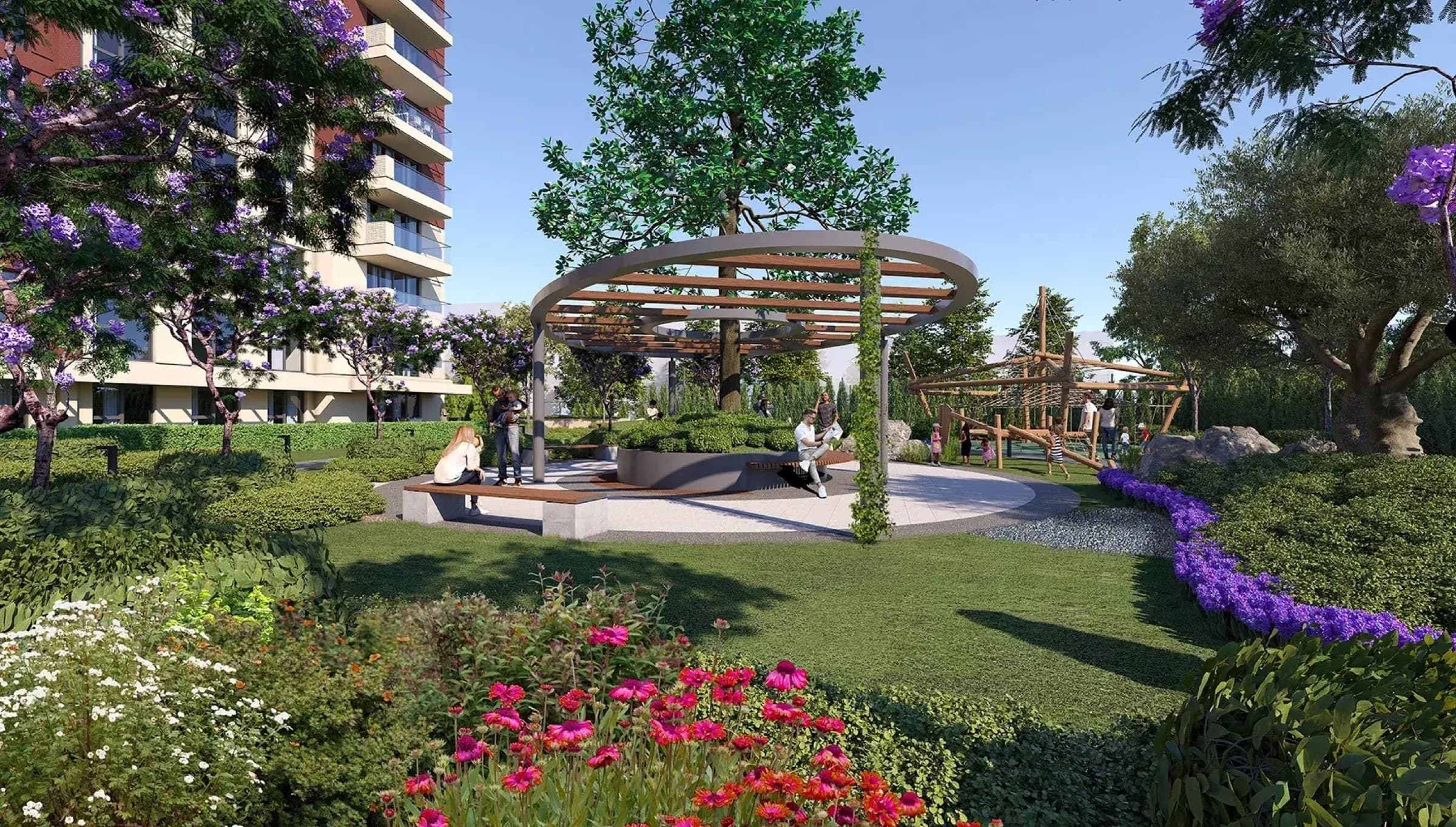 Hayat City'nin ortak bahçesinin merkezinde dairesel ahşap pergola ve kavisli banklar; arkada çiçek tarhları, çim ve çocuk tırmanma oyuncağı, Bağcılar, İstanbul