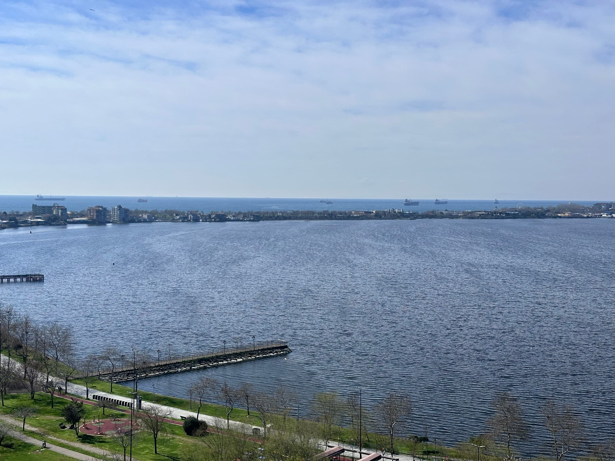 The lakeside park below Kırımlı Park, its promenade, playground and pier along the water, with Küçükçekmece Lake opening to the Marmara Sea beyond