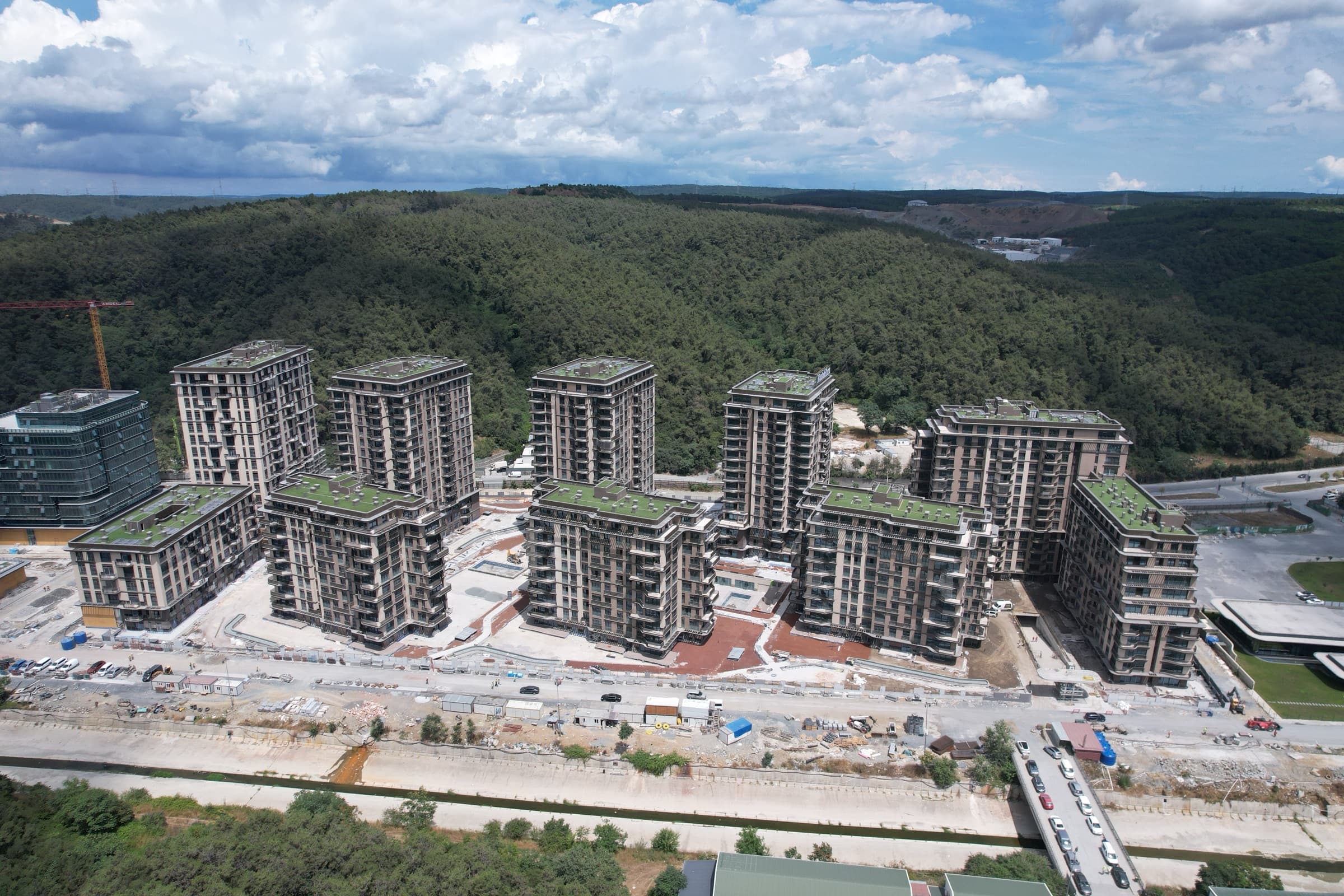 İnşa halindeki Maslak Koru, havadan fotoğraflandı: bloklar çıplak betonla kaba inşaatı bitmiş ve bitkilendirilmiş çatı terasları çoktan serilmiş, zeminde şantiye yolları ve paravanlar hâlâ yerinde, arkada kareyi dolduran Belgrad Ormanı.