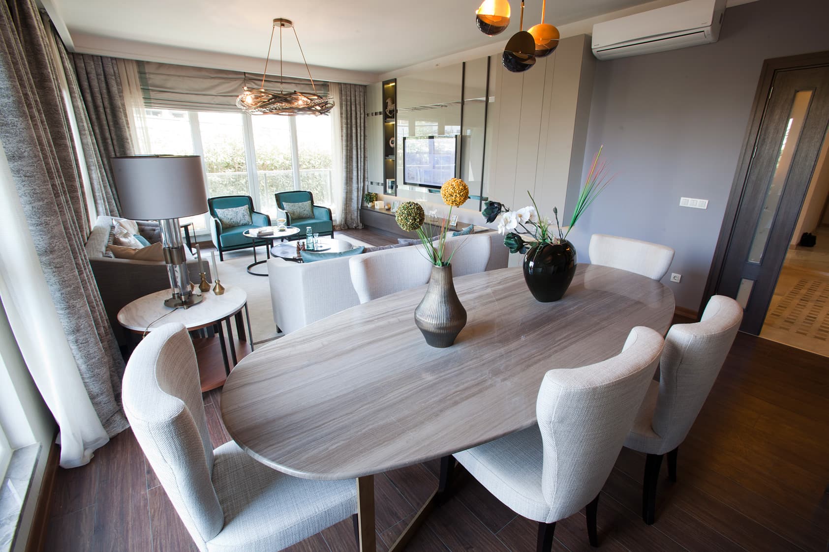 The dining area of a furnished Nidapark Küçükyalı show apartment, with an oval stone-topped table for six opening onto the living room and the balcony beyond.