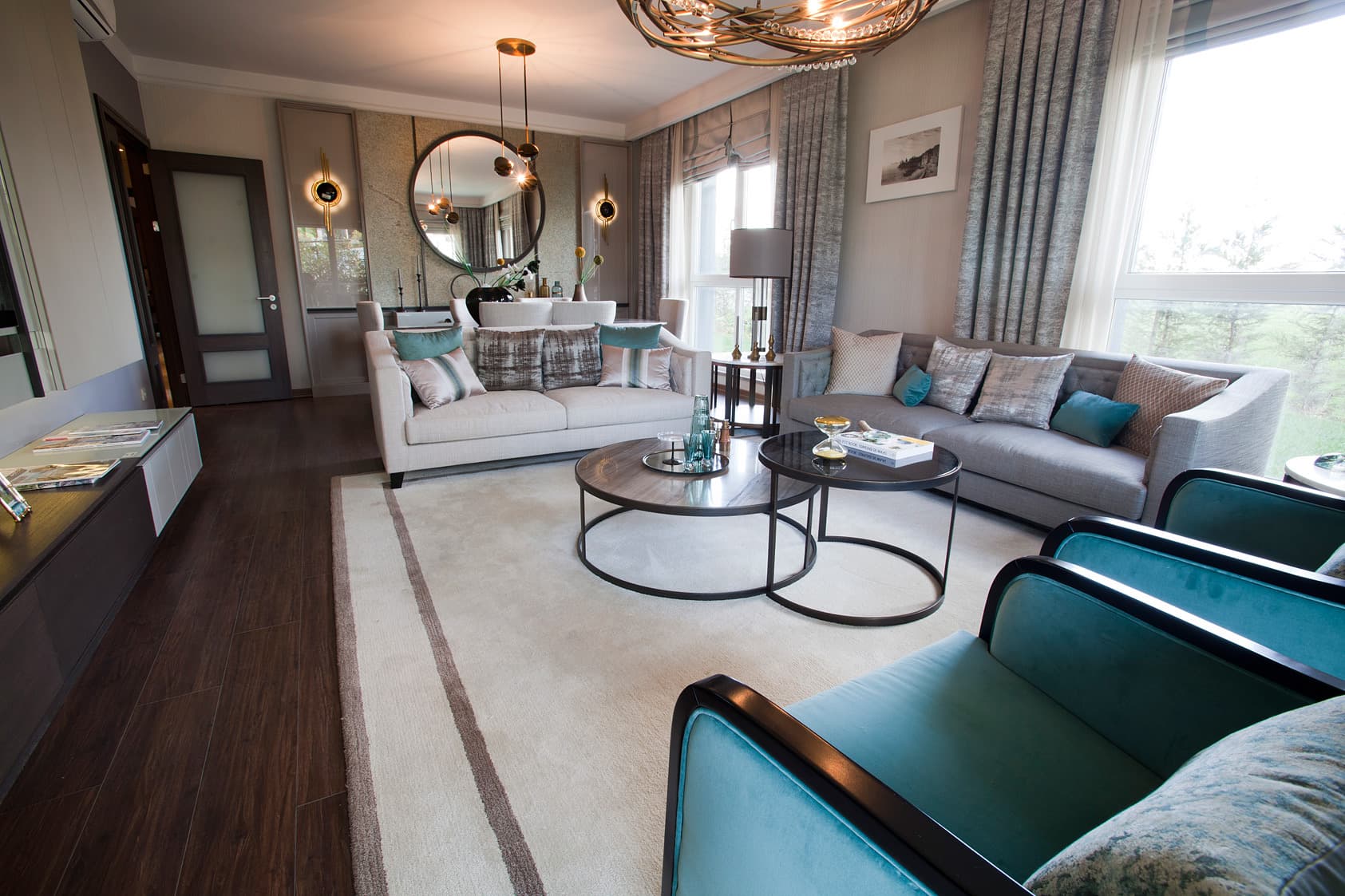 The living room of a furnished Nidapark Küçükyalı show apartment, with facing sofas, teal armchairs, a circular mirror and full-height windows onto the gardens.