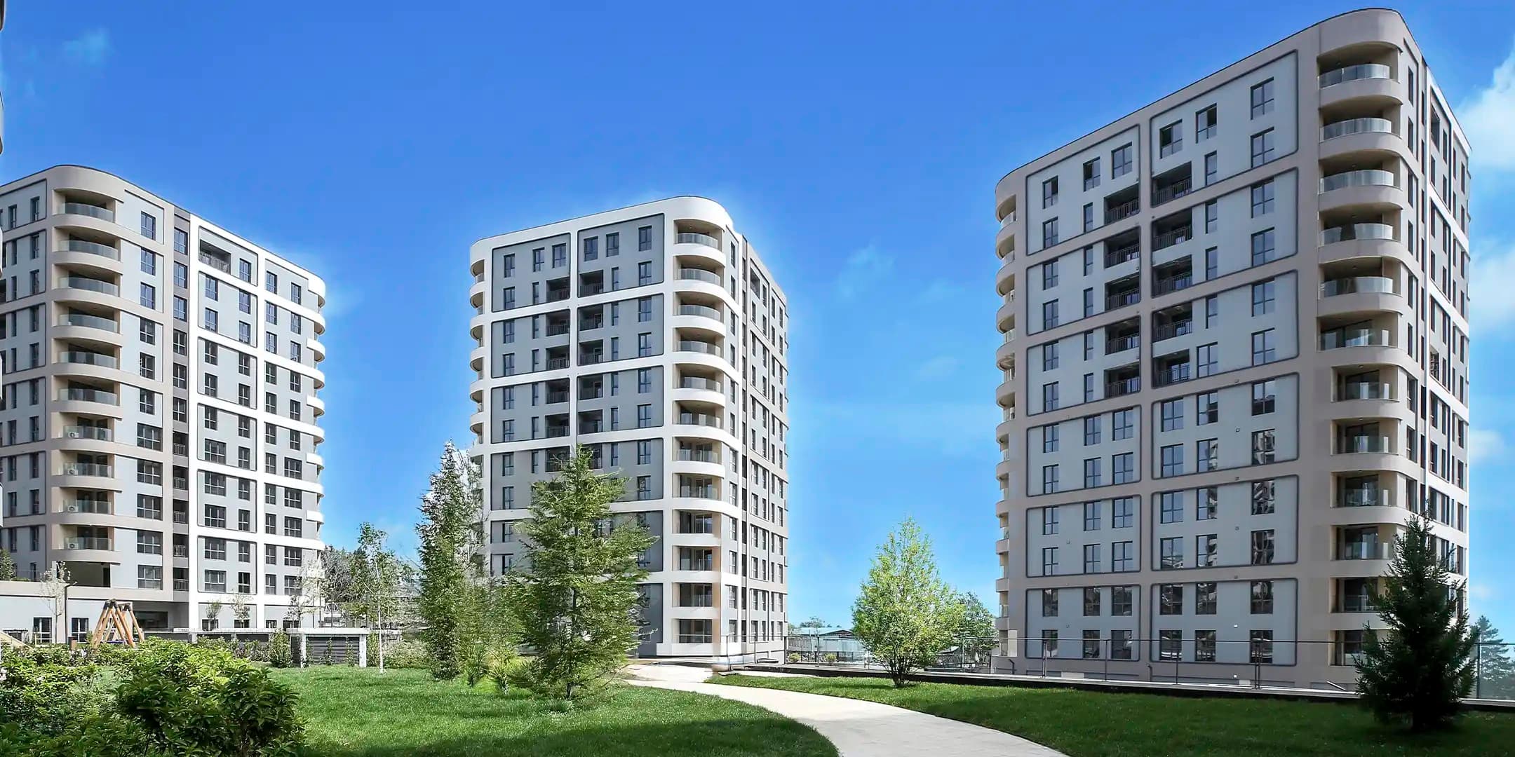 ثلاث كتل شقق منجزة في RAMS City Haliç عبر المرج، وأطراف شرفات منحنية متراكبة على كل واجهة وأشجار فتية ما زالت مدعومة عند أقدامها