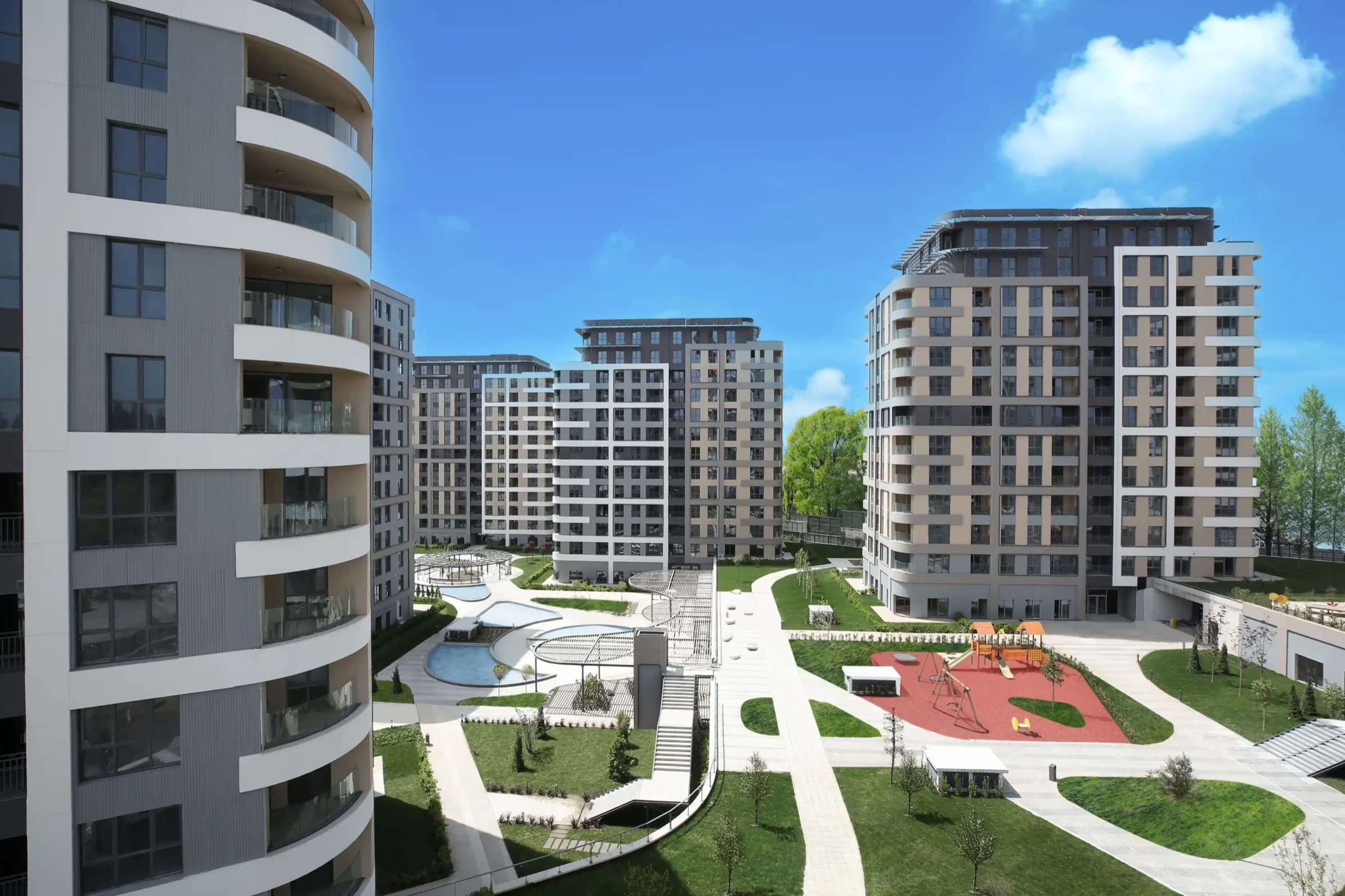 النظر إلى فناء RAMS City Haliç من طابق علوي: قناة مياه منحنية، وعرائش، وملعب مطاطي أحمر، وممرات فاتحة ممدودة بين الكتل المنجزة