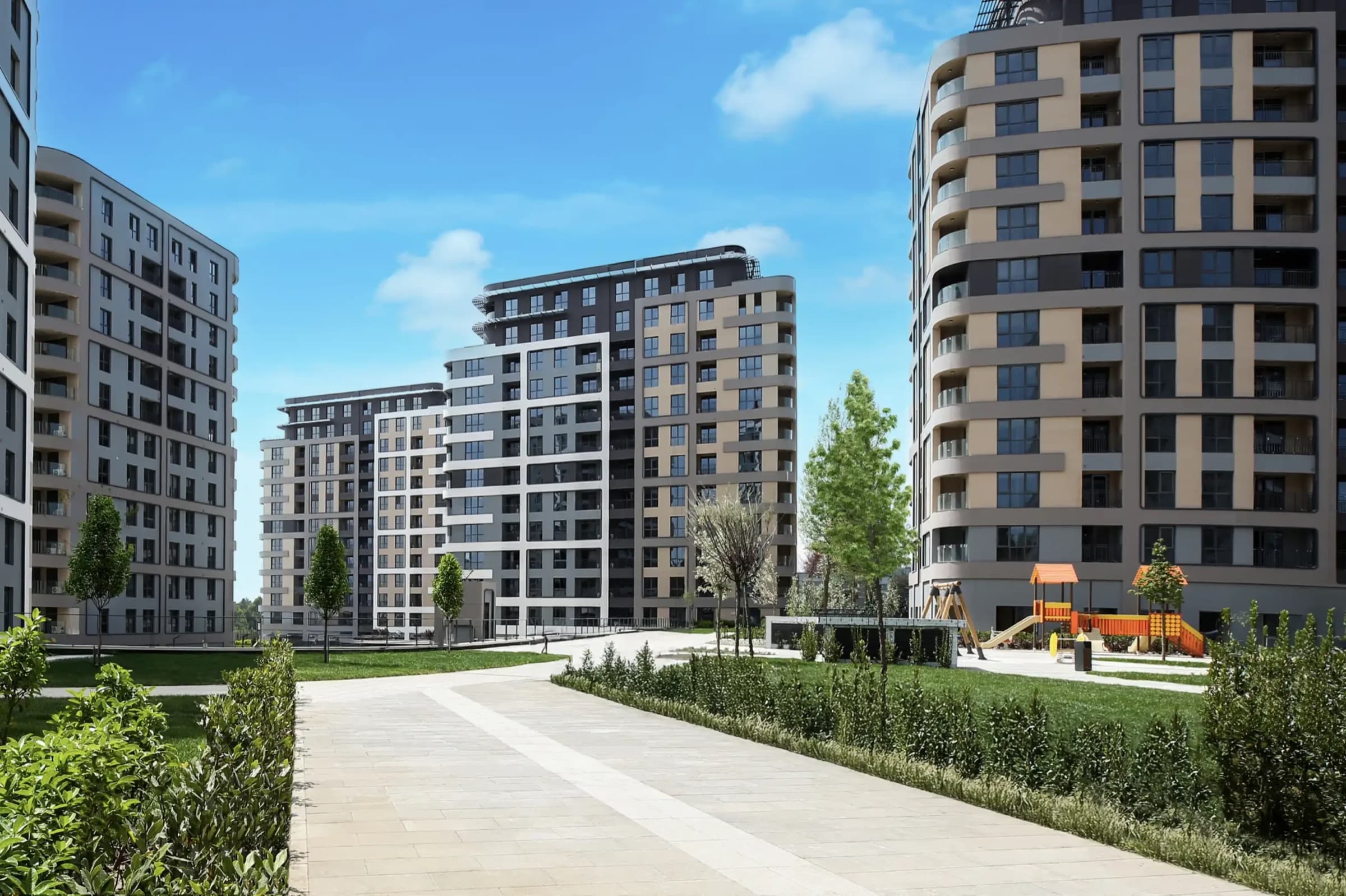ممشى حجري عريض يمتد بين كتلتين مكتملتين في RAMS City Haliç، بسياجات نباتية مشذّبة على الجانبين وهيكل لعب خشبي للأطفال إلى اليمين