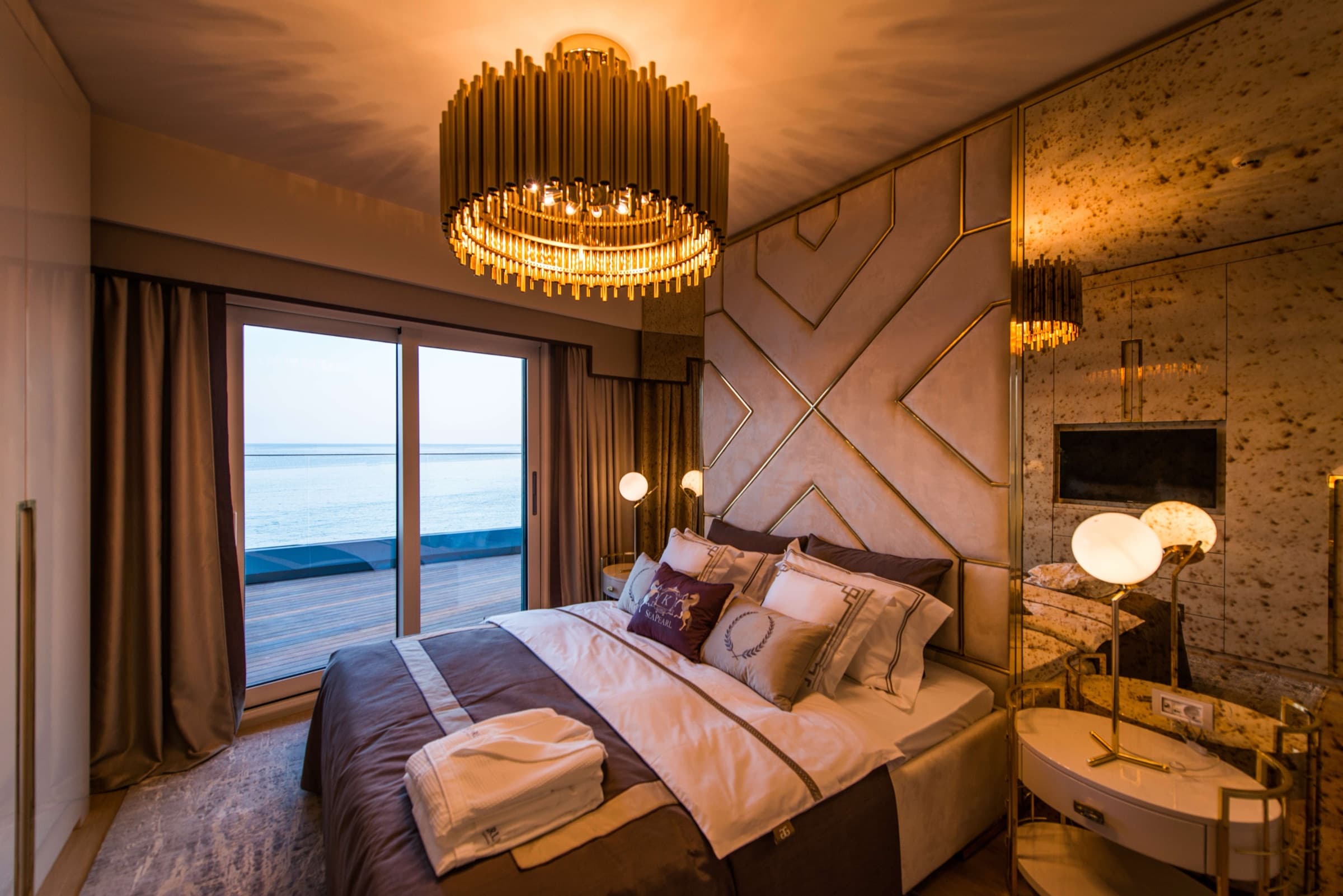 A bedroom in a sea-facing residence at SeaPearl Ataköy, the Marmara Sea and the shoreline visible through the full-height glazing beside the bed