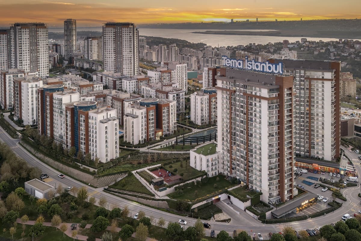 Aerial view of Tema İstanbul at golden hour, the project's rooftop sign above its blocks and open water on the horizon