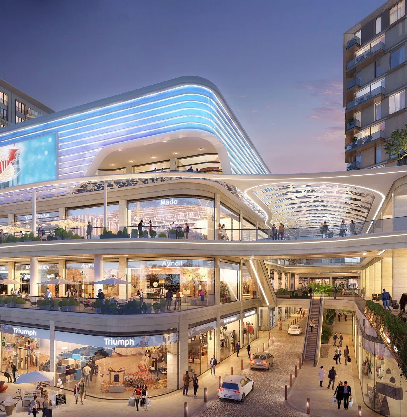 Dusk view of the development's curved multi-level shopping centre, its glowing blue light bands over glazed shopfronts including Mado, Triumph and a cinema sign, with cafe terraces, escalators and a residential tower behind — artist's impression