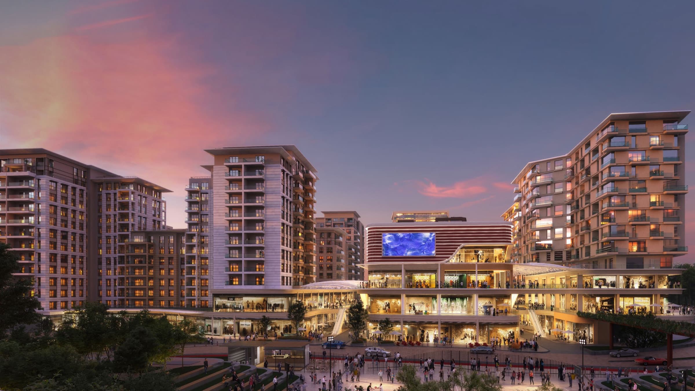 Wide computer-generated dusk view of the development under a pink sky, the lit shopping terraces and their media screen at the centre with the residential blocks ranged around and a busy public square below — artist's impression