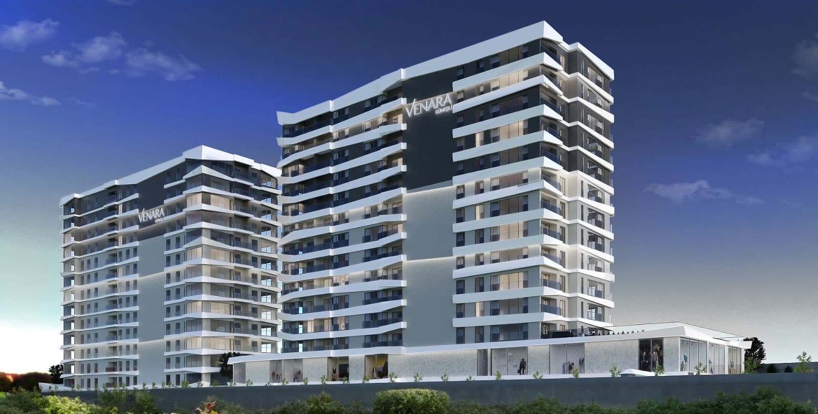 The two blocks of Venara Güneşli at dusk, the project name illuminated on each flank, tiered balconies running the length of both elevations, and the glazed commercial units lit along the base at street level.