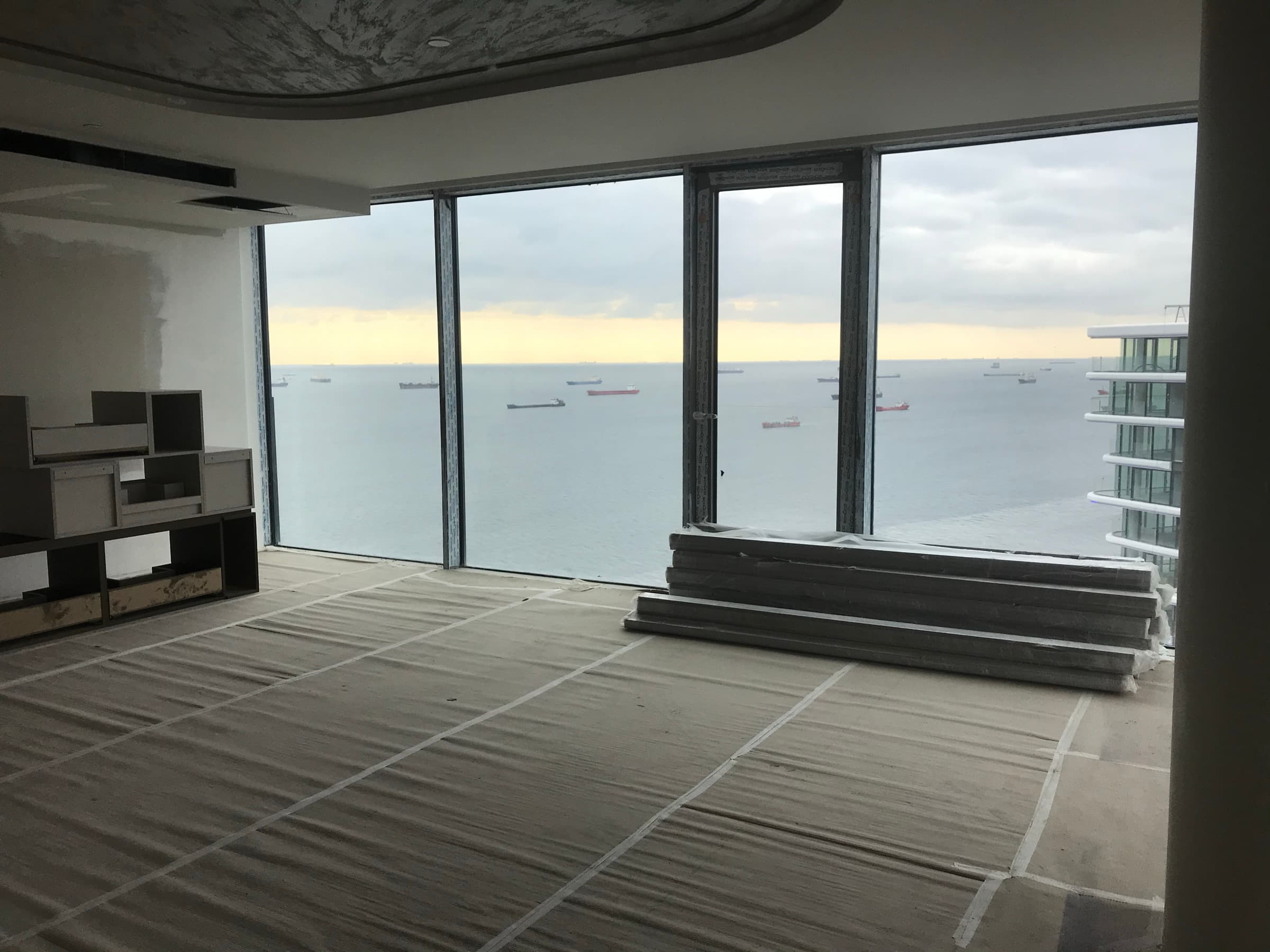 The Sea of Marmara seen through the full-height glazing of a residence at Yedi Mavi during fit-out, cargo ships at anchor offshore and the floor still under taped protective sheeting