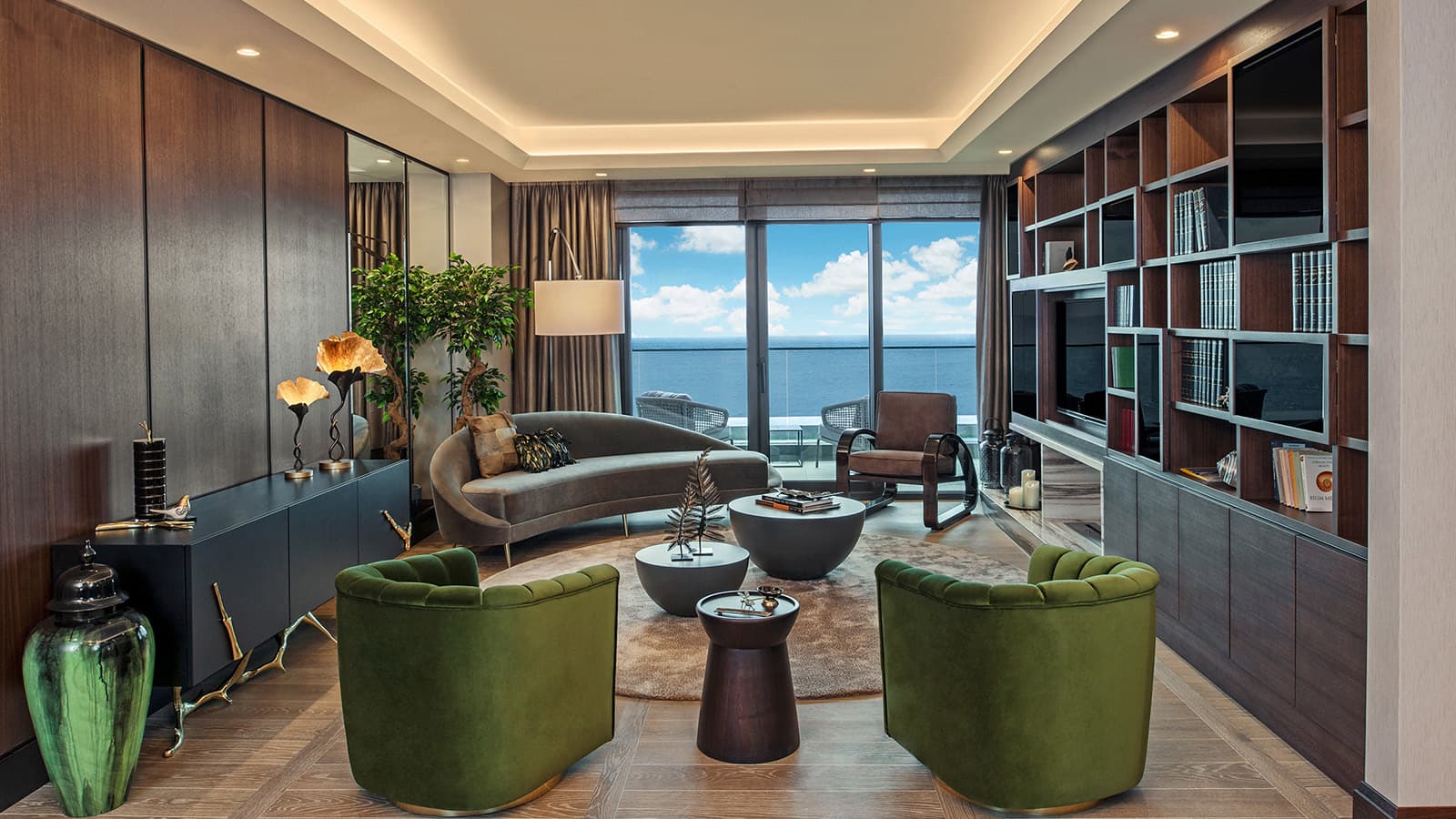 Living room with green velvet armchairs and a curved sofa facing a sea-view balcony