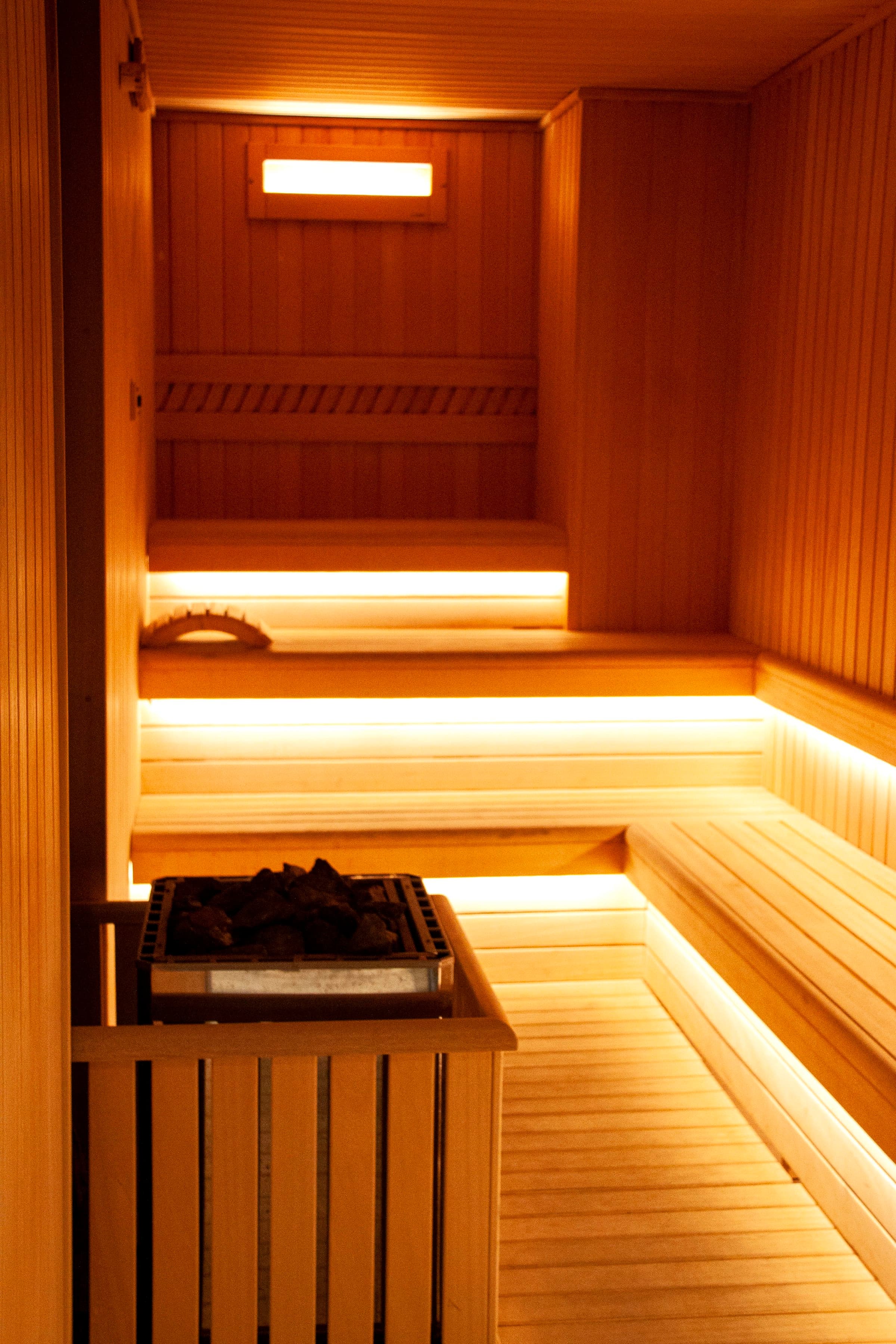 Sauna interior with tiered timber benches, under-bench lighting, and a stone-topped heater